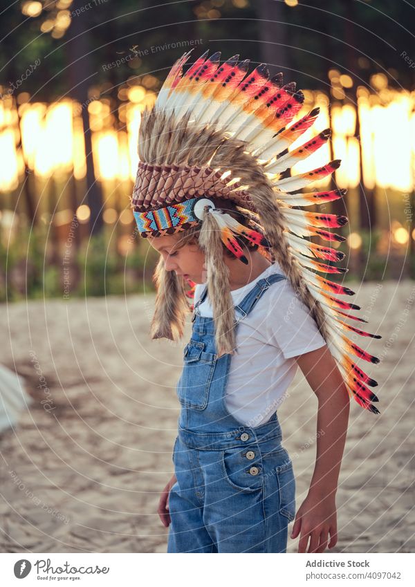 Content kid in authentic hat by tent boy wigwam indian feather content delighted overalls denim standing crossed arms portugal park leisure playhouse childhood