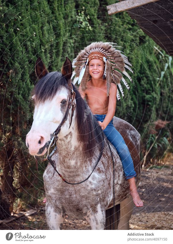 Happy child saddling stallion boy horse ride authentic saddle war bonnet indian costume training native art headdress head wear hat feather park countryside