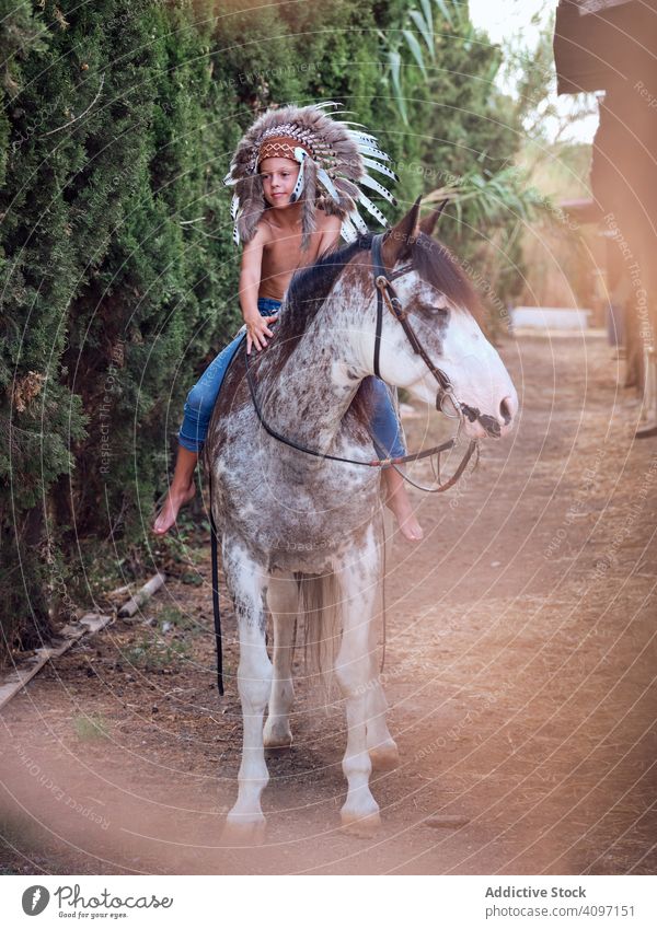 Concentrated child saddling stallion boy horse ride authentic saddle war bonnet indian costume training concentrated native art serious headdress head wear hat