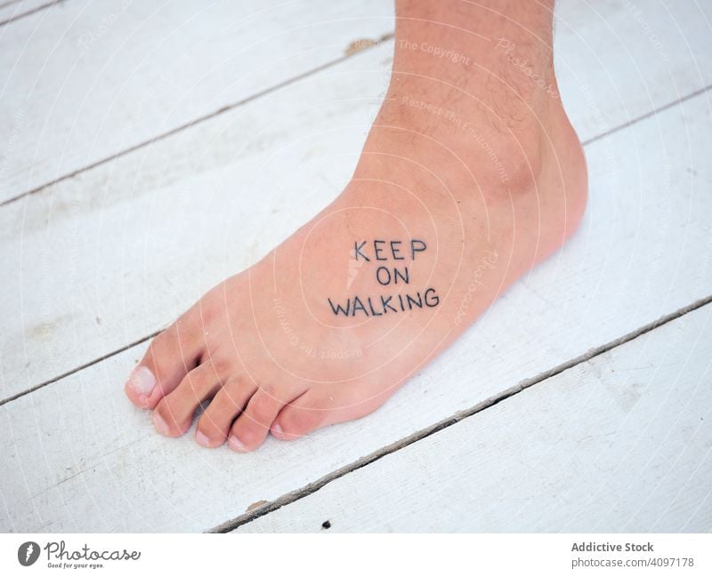 Foot with motivational tattoo on wooden floor person writing stand barefoot keep on walking pier white inspiration resort inscription leg body part lumber