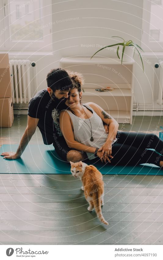 Loving couple cuddling on floor while cat walking around cuddle loving embrace tender sit ginger hipster modern minimalistic moving home relocation apartment