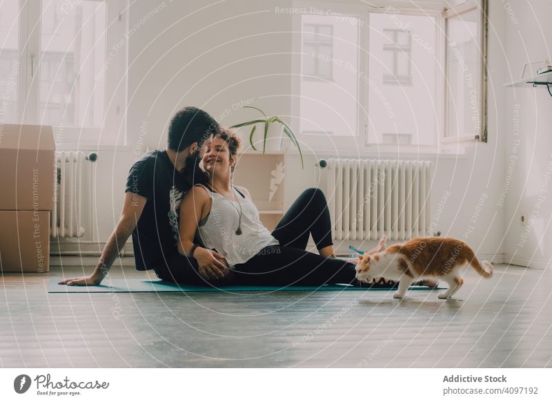 Loving couple cuddling on floor while cat walking around cuddle loving embrace tender sit ginger hipster modern minimalistic moving home relocation apartment