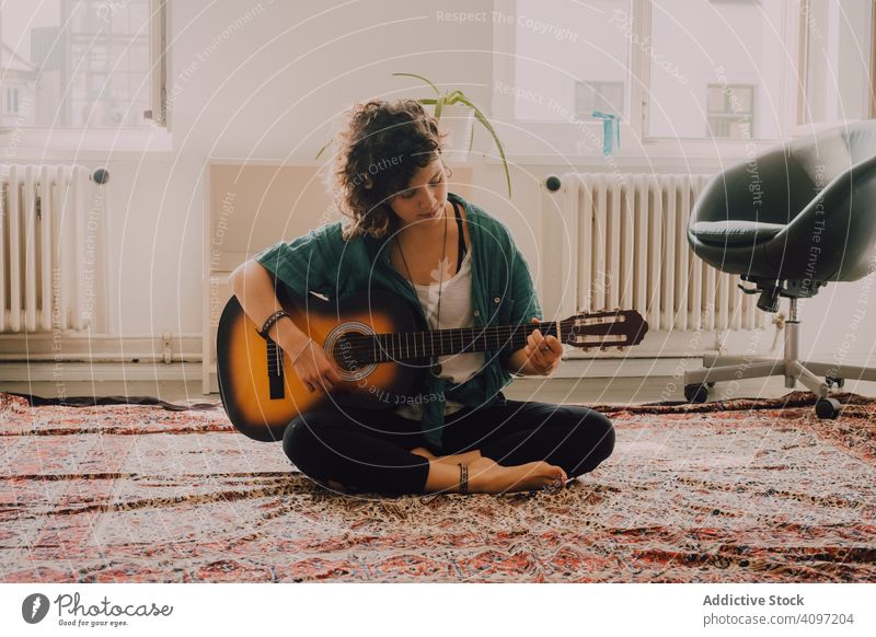 Content woman playing guitar at home content relaxed casual acoustic minimalistic room floor sit musician guitarist crossed legs young adult leisure fun