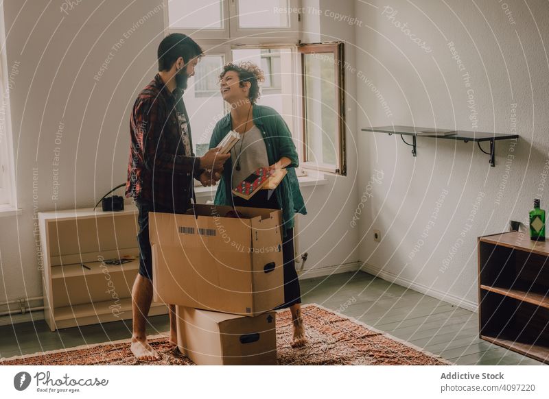 Casual couple unpacking boxes in apartment laughing casual hipster together barefoot room light domestic home house cardboard new carton relocation estate
