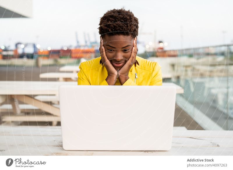Female working on laptop at table woman using desk city african american jacket yellow female wooden young casual workplace busy remote freelance surfing