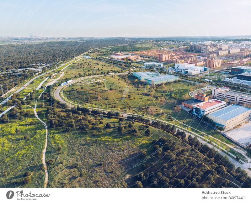 Picturesque distant urban city surrounded with fields and forest suburb highway drone view aerial industrial modern road green grass wood tree summer horizon