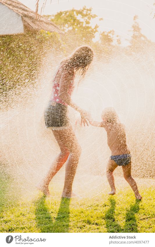 Sisters having fun under spraying water sister lawn play run sunny daytime yard together teen kid child girl happy vacation weekend lifestyle leisure joy wet