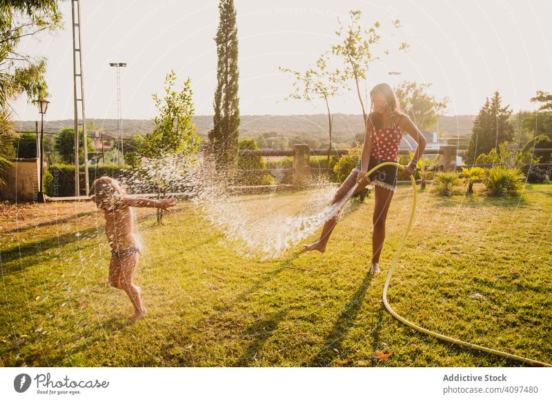 Teen girl spraying little sister in garden fun water lawn hose sunny daytime yard together teen kid child happy cheerful play vacation weekend lifestyle leisure
