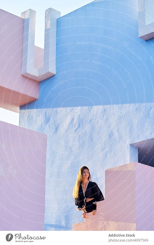 Woman standing on modern blue building woman long hair dress black elegant barefoot construction structure geometric architecture urban facade center wall