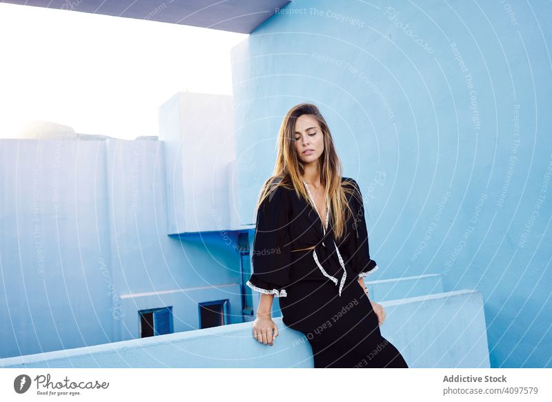 Woman leaning on modern blue building woman long hair dress black elegant standing construction structure geometric architecture urban facade center wall