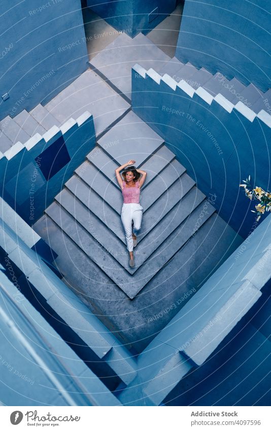 Woman lying on modern blue building woman casual floor stairs downstairs elegant construction structure geometric architecture urban facade center wall abstract