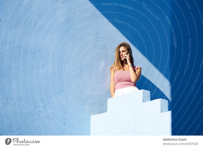 Woman on a blue building using smartphone woman casual elegant construction stairs structure geometric architecture urban facade wall abstract maze public