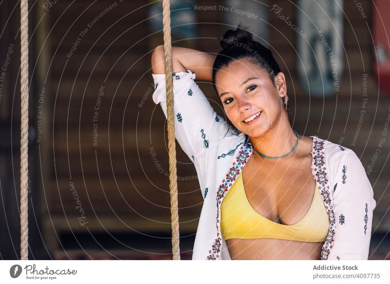 Cheerful woman riding on swings on tropical terrace ride cheerful smile tanned happy casual sit rest wooden wall costa rica young adult youth fun enjoyment