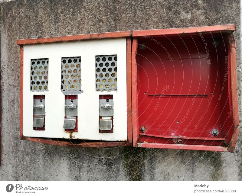 Ramped old red chewing gum machine on grey house wall in Lemgo near Detmold in East Westphalia-Lippe Vending machine Gumball machine Red Tin Old tattered dented