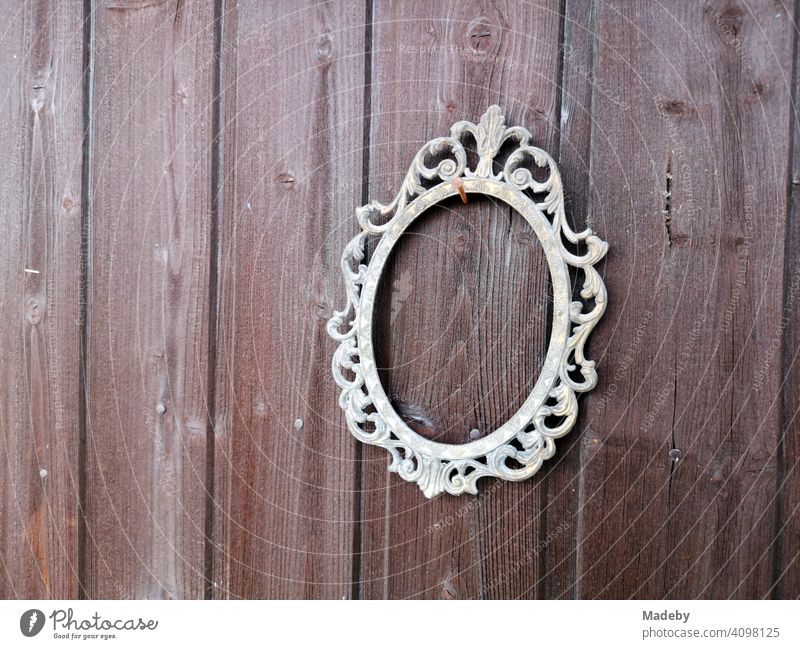 Ornate oval metal picture frame without picture on a rusty nail on the outside of a brown wooden hut in the harbor garden in Offenbach am Main in Hesse, Germany