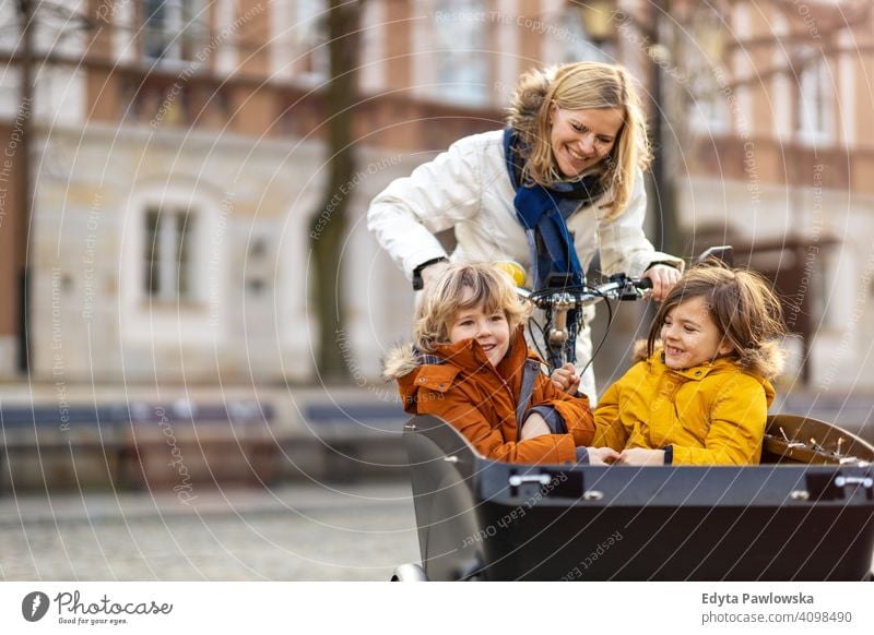 Mother checking on her children who is riding in the front section of a cargo bike cycling transport tricycle healthy active bicycle biking modern