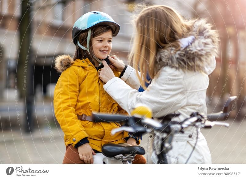 Mother putting bicycle helmet on her son young wearing bike cycling winter woman autumn mother family parents relatives boy kid children relationship together