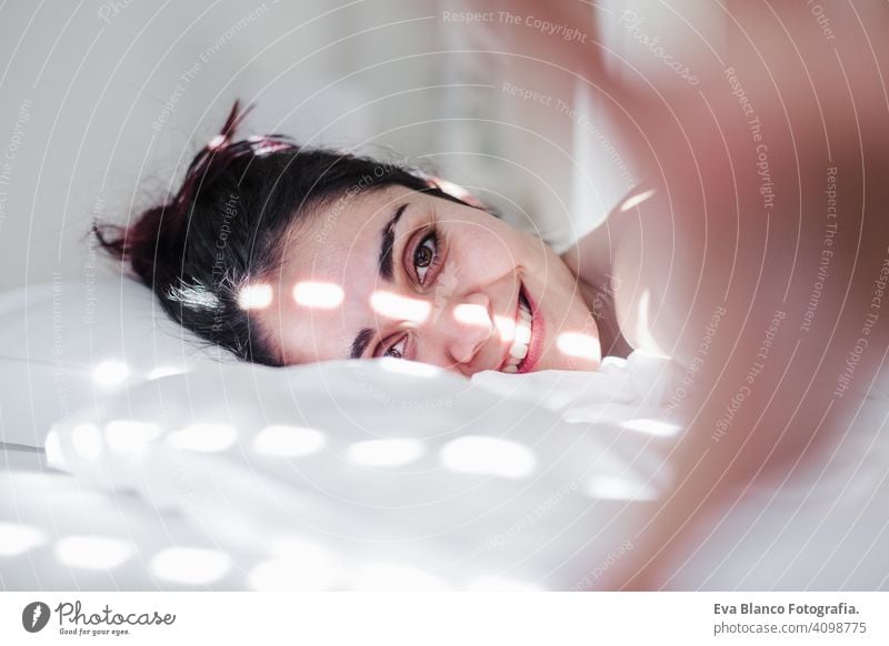 portrait of attractive young caucasian woman relaxing in bed during morning time. Lady enjoys fresh soft bedding linen and mattress in bedroom sleeping nap