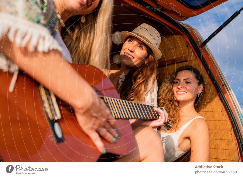 Cheerful women with music instrument resting in car during road trip travel friend guitar song happy van play journey tourism laugh adventure vacation cheerful