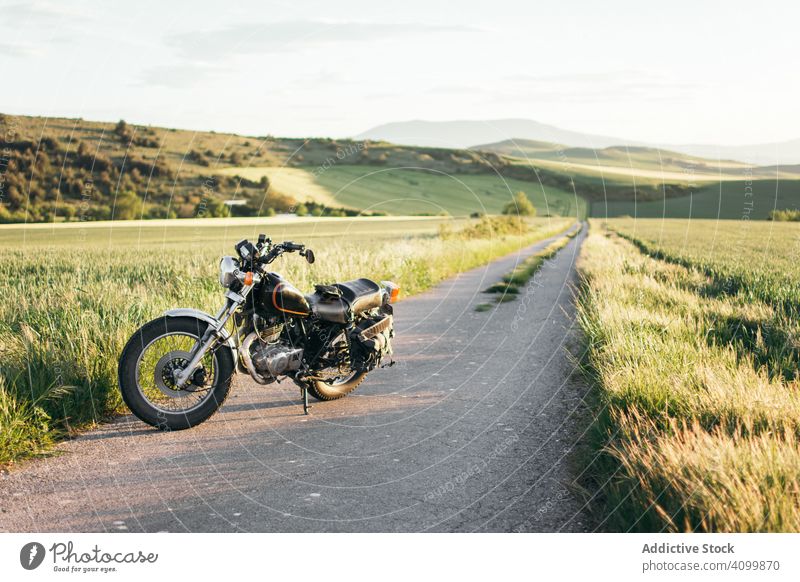 Motorcycle on countryside road near grass motorcycle field sunny daytime peaceful asphalt motorbike path vehicle transport way meadow modern contemporary nobody