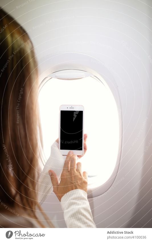 Woman turning on smartphone nearby window in plane flight using browsing woman surfing mobile passenger trip device gadget airplane female vacation aircraft