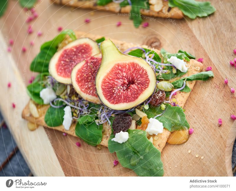 Portions of delicious sandwich with figs and cheese on cutting board open sandwich crisp bread rocket salad fresh fruit food meal refreshment rye bread exotic