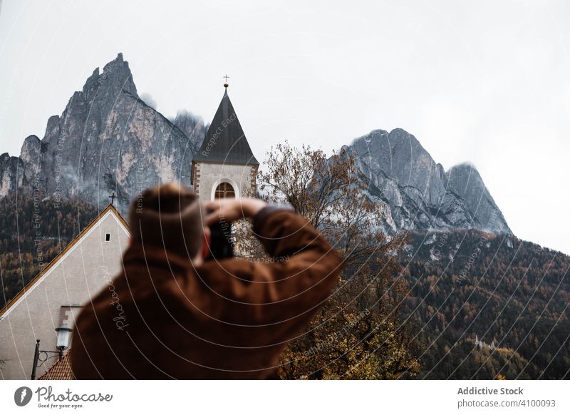 Male traveler making photo of nature and church on camera tourist taking building landscape mountains dolomites italy forest cliff rock sky photographing