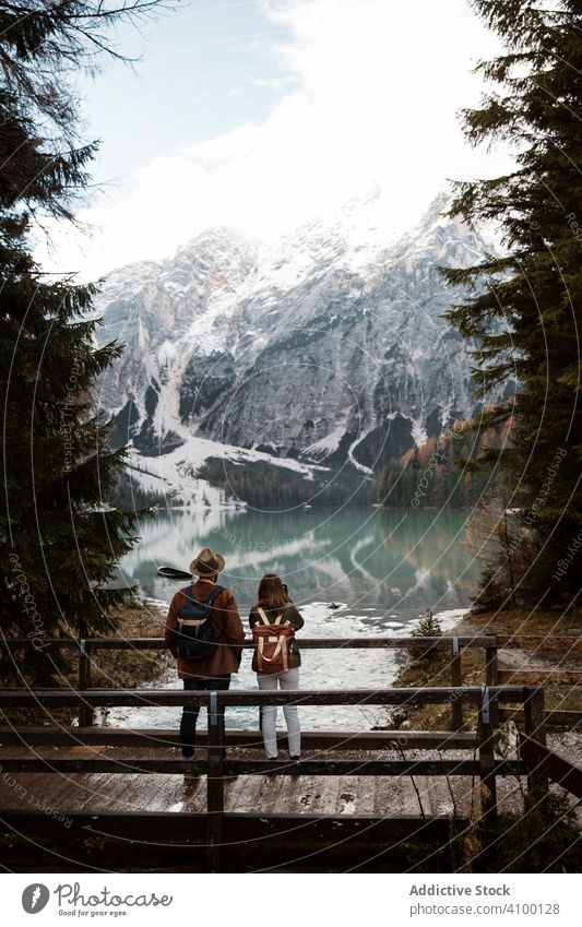 Resting couple taking photo of lake and mountains pine tree forest sky standing wooden bridge casual nature adventure rock activity landscape lifestyle track