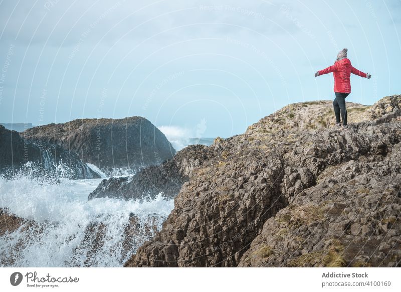 Woman on top of rock with sea surf woman cliff edge raging stormy splash coast water waves blustering crag marine highland climb female ballintoy antrim
