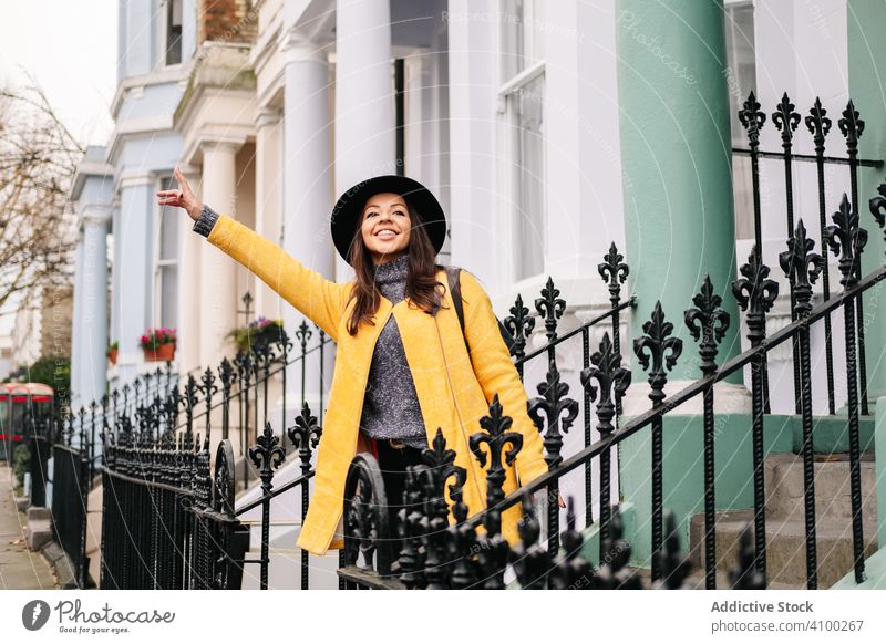 Cheerful woman hailing cab on street catch waving hand house smile stylish london united kingdom female city town taxi coat hat cheerful happy passenger