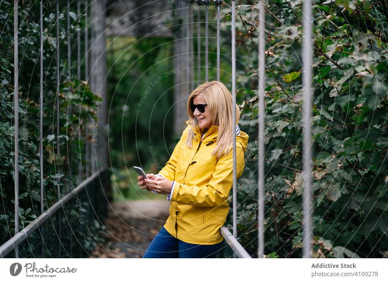 Happy female traveler taking selfie on suspension bridge in summer footbridge smartphone woman forest cellphone happy hanging holiday lifestyle tourist vacation