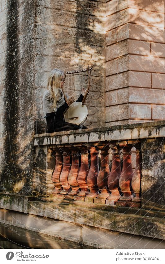 Focused woman playing lyre on aged terrace romance instrument ballade old musical stone building talented historical sunny female art musician classic