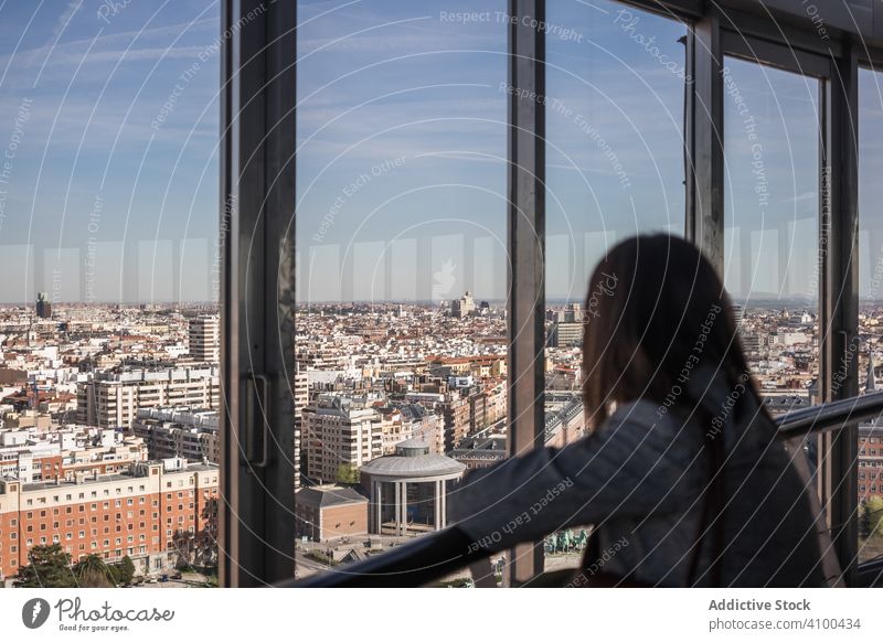 Anonymous woman looking out balcony window city admire apartment rest modern home sunny daytime female relax lifestyle lean railing young town urban flat lady