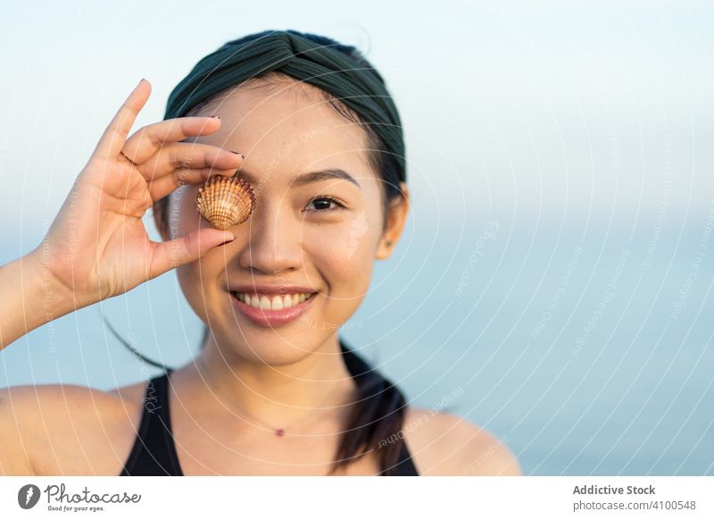 Happy Asian woman covering eye with sea shell sportive beach fit happy smile asian cheerful joyful active female ethnic summer enjoy healthy athletic