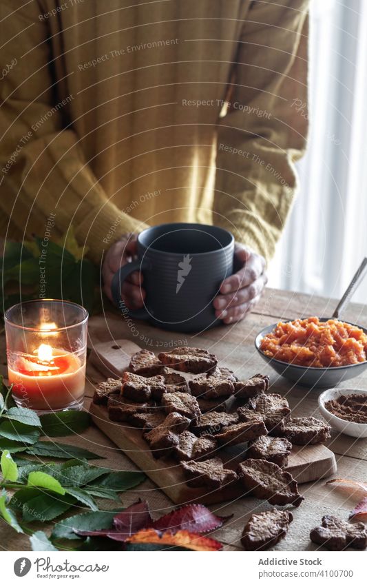 Crop person enjoying hot beverage and cookies drink warm home candle cozy leaf dessert table mug morning pastry comfort biscuit cup sweater snack treat sugar