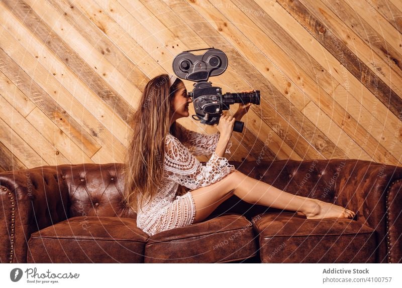 Young woman recording video with a vintage camera cinema videography videographer wood couch antique device camerawoman concept brown hipster filming funny