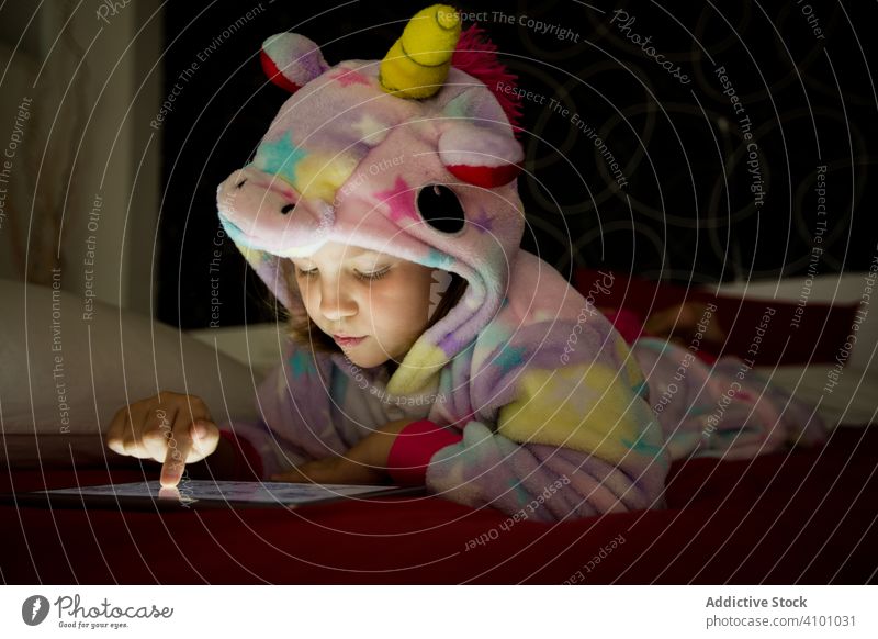 Girl using tablet on bed girl kigurumi unicorn blanket hide watching playing bedtime pajama lying child happy fun positive enjoy red white kid preschooler cute