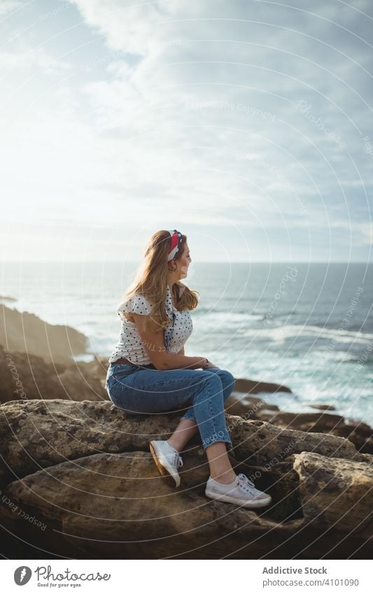 Pensive woman sitting on stone and looking at seascape dreamy coast pensive horizon freedom inspiration harmony seaside rock ocean cloudy sky style shore calm