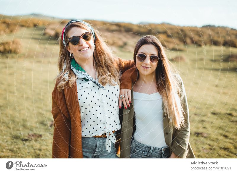 Stylish cheerful women standing on green field happy sister harmony countryside spring together nature close travel tourism journey activity adventure