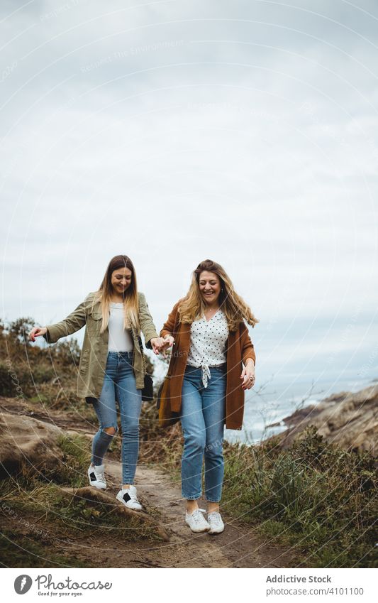 Happy female friends walking on trail at seaside women hill sister mountain countryside together support slippery happy smile cheerful laugh enjoy path footpath