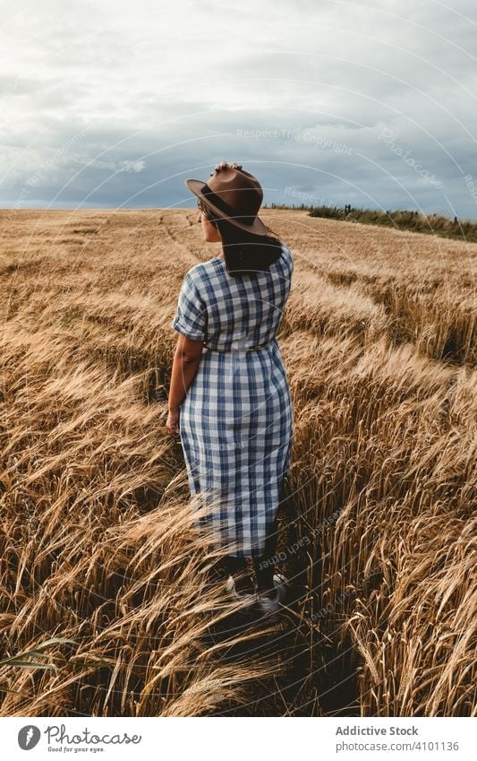 Anonymous woman standing dry field summer grain hat rest sunny daytime female adult nature countryside meadow lifestyle relax harmony idyllic lady weekend grass