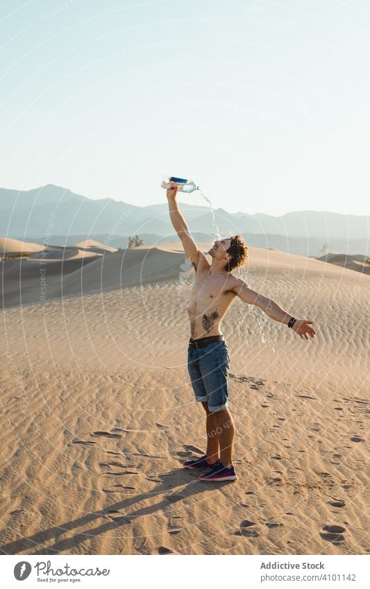 Thirsty man with naked torso drinking water stretching hands in desert dunes travel thirsty pouring vacation direction holiday sand summer freedom land tourism