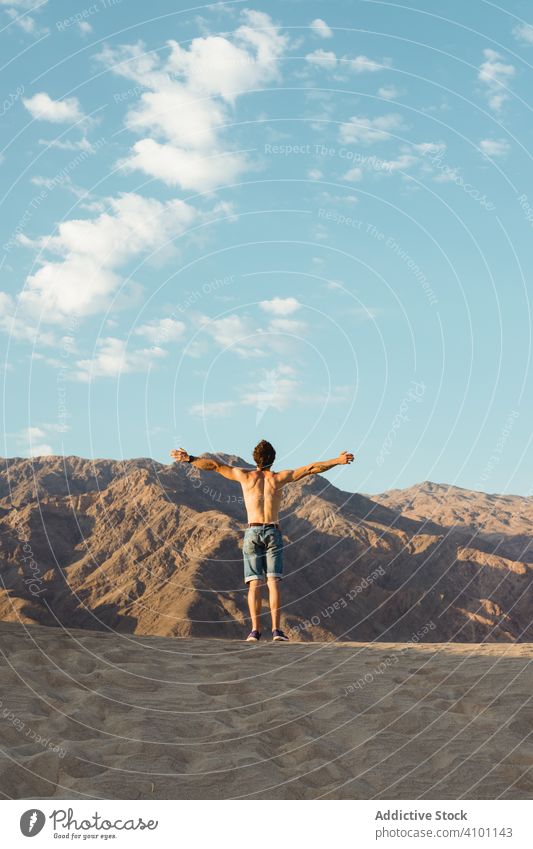 Back view of active young man without shirt enjoying wind in dry Death Valley desert dunes travel naked torso pouring stretching vacation direction holiday sand