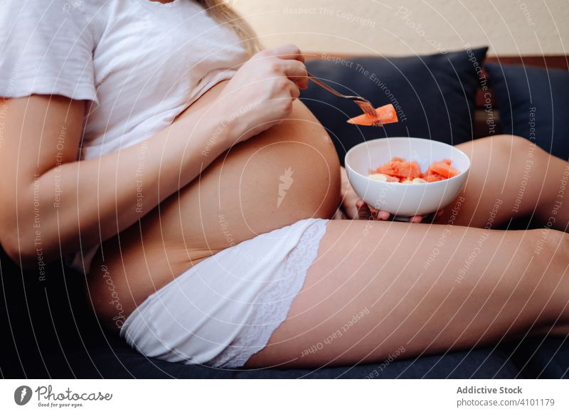 Faceless pregnant woman eating fruits with fork pregnancy maternity mother food baby nutrition belly health young fresh female expect wait care piece slice