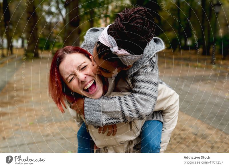 Joyful multiracial girlfriend piggybacking in autumn park couple embracing bonding smiling relationship together lgbt homosexual horizontal romantic cheerful