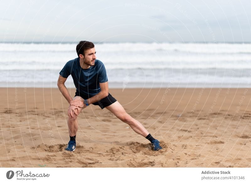 Male athlete in active wear doing exercises on legs at empty beach sportsman training workout stretch lunge fit lifestyle healthy male athletic sea ocean water