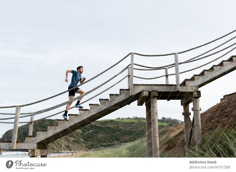 Sportsman running on stairs at shore with mountains sportsman upstairs beach hillside sky train workout healthy lifestyle fit slim step athletic active warm up