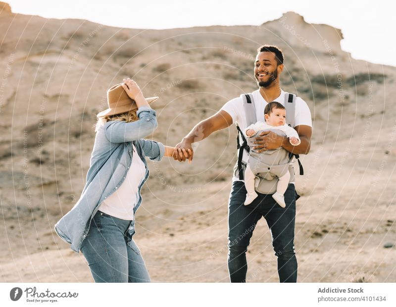 Diverse parents dancing while walking with baby dance family happy smile sand desert carry fun nature newborn cheerful lifestyle modern child wife bonding love