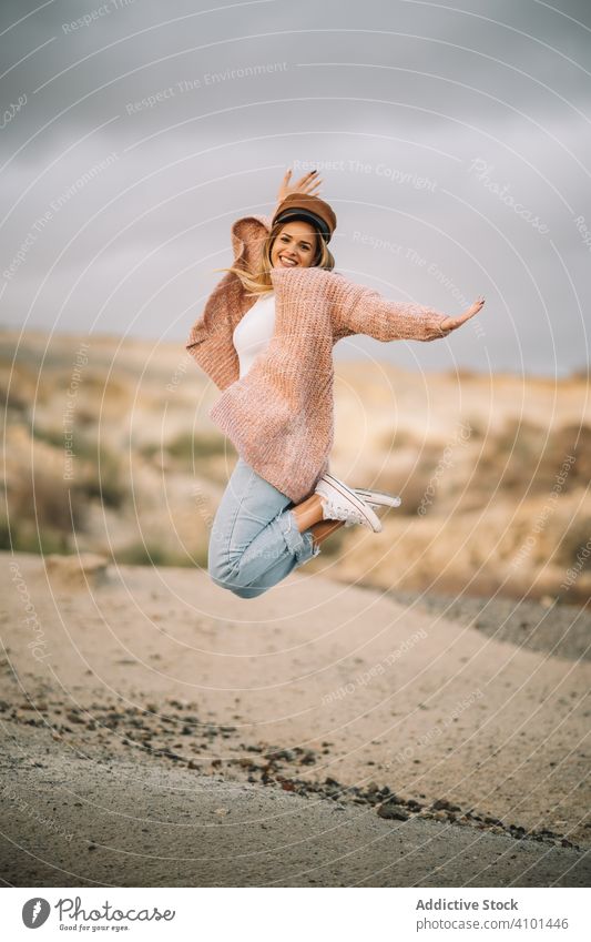 Cheerful woman jumping in desert landscape sand smile high cheerful vacation happy style blonde female up freedom active fun young bent legs holiday nature