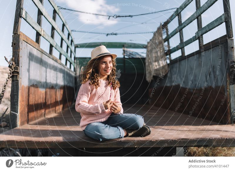 Focused girl resting in truck body focused concentration car hand on knees pensive think planning thoughtful rose jumper casual straw hat smile content